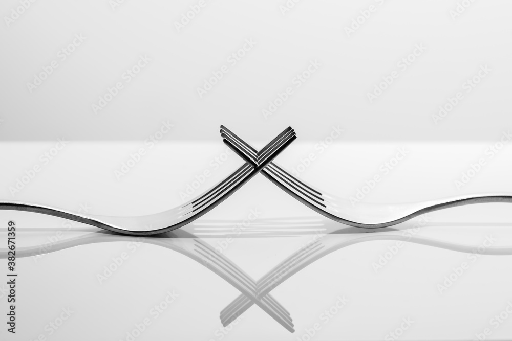 Two forks with reflections on light background, closeup with selective focus - black and white