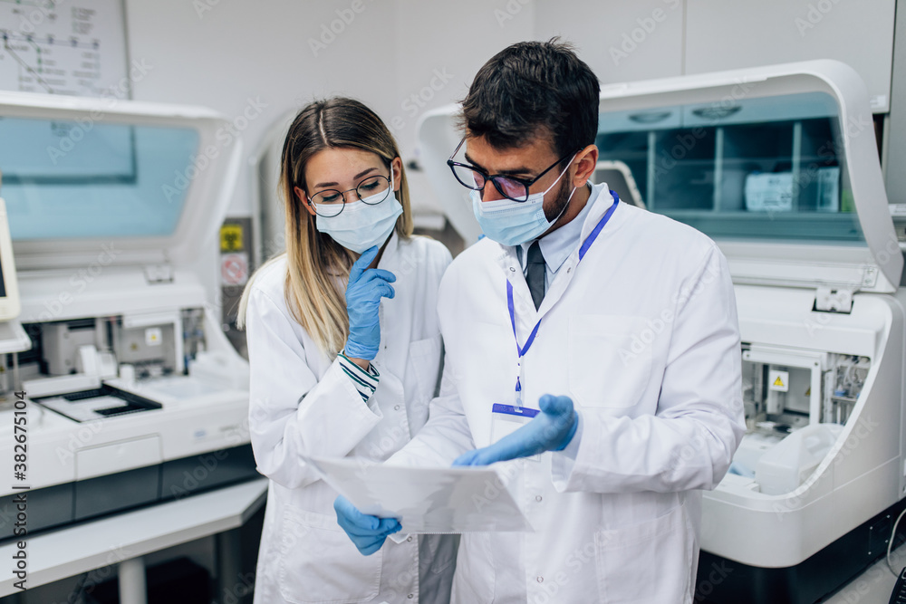 Two scientists or technicians with face protective masks work in laboratory on human blood samples. Two scientists or technicians with face protective masks work in laboratory on human blood samples.