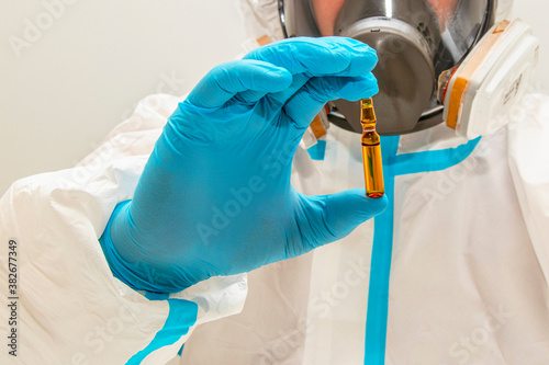 The medicine. Close-up. A doctor in protective overalls, a mask and gloves holds an ampoule with a vaccine against the virus in his hand.