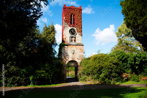Sticker vintage brick clocktower with red ivy, surrounded by green bushes or hedges in S