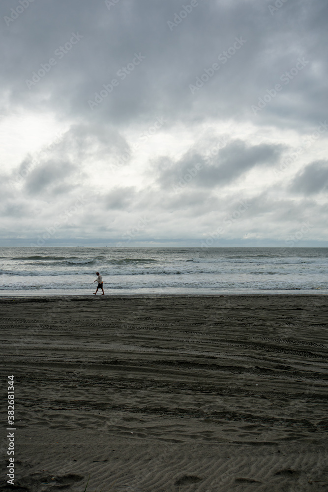 A Lonely Man Walking Across the Beach With A Dramatic Stormy Sky Behind Him