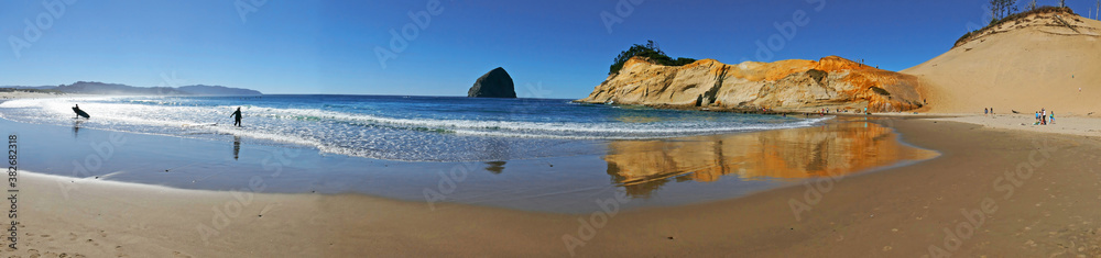 A panorama of the beach at Pacific City, Oregon. Several surfers are preparing to ride the waves. Haystack Rock and a headland stand on the horizon. A panorama of the beach at Pacific City, Oregon. Several surfers are preparing to ride the waves. Haystack Rock and a headland stand on the horizon.