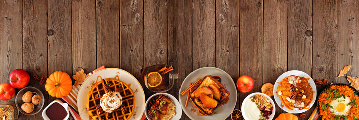 Assortment of autumn breakfast or brunch items. Bottom border against a dark wood background. Pumpkin spice pancakes, waffles, apple french toast, oatmeal, egg skillet, yogurt. Top view. Copy space.