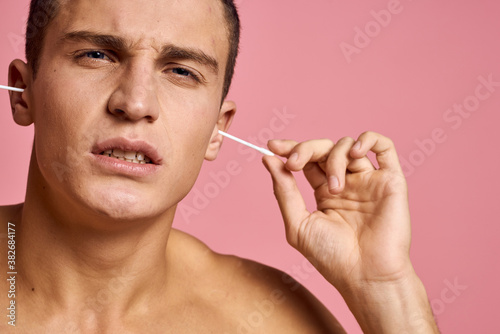 Emotional man with ear sticks in hands on pink background emotions cropped view of naked torso