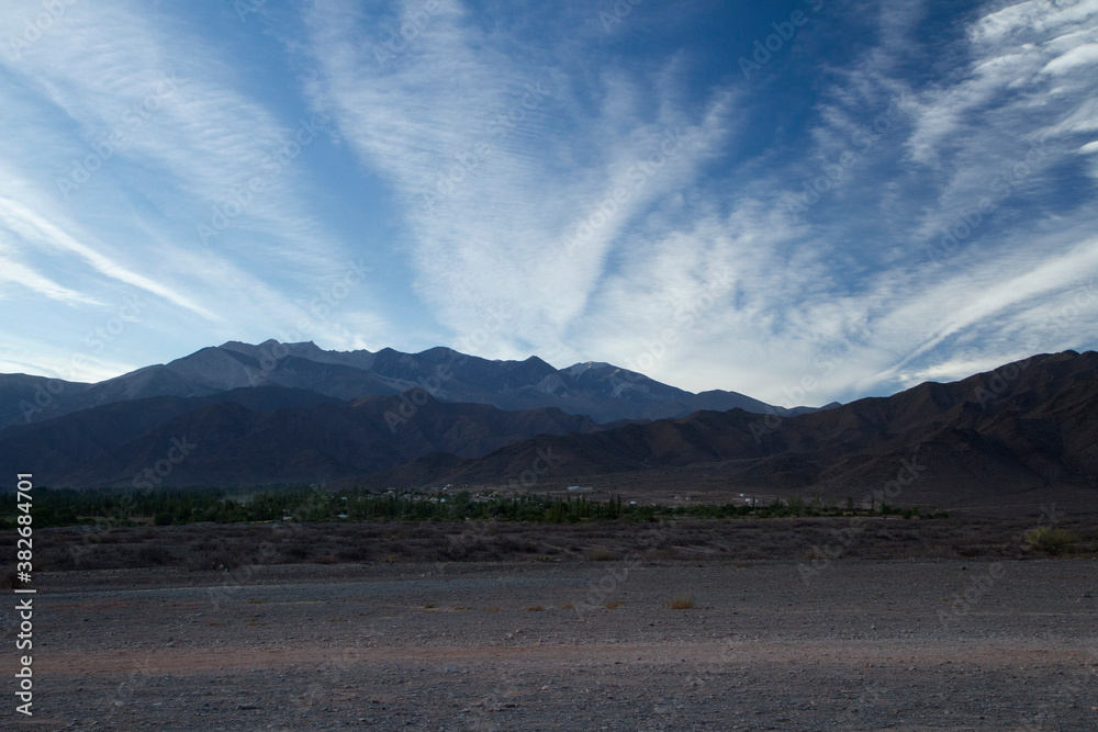 Beautiful sunrise in the mountains. Panorama view of the dirt road along the desert and Andes mountain range with beautiful dawn colors under a deep blue sky with clouds.