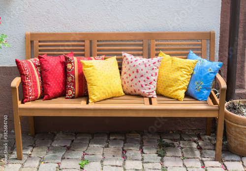 Wood bench outside with much multicolor pillows. photo