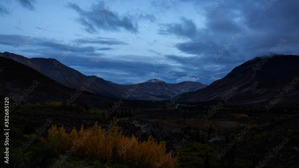 Time Lapse. View of Scenic Road from Above surrounded by Trees and Mountains during Fall in Canadian Nature. Cloudy Sunset. Aerial View. Taken in Tombstone Territorial Park, Yukon, Canada. Zoom Out Time Lapse. View of Scenic Road from Above surrounded by Trees and Mountains during Fall in Canadian Nature. Cloudy Sunset. Aerial View. Taken in Tombstone Territorial Park, Yukon, Canada. Zoom Out