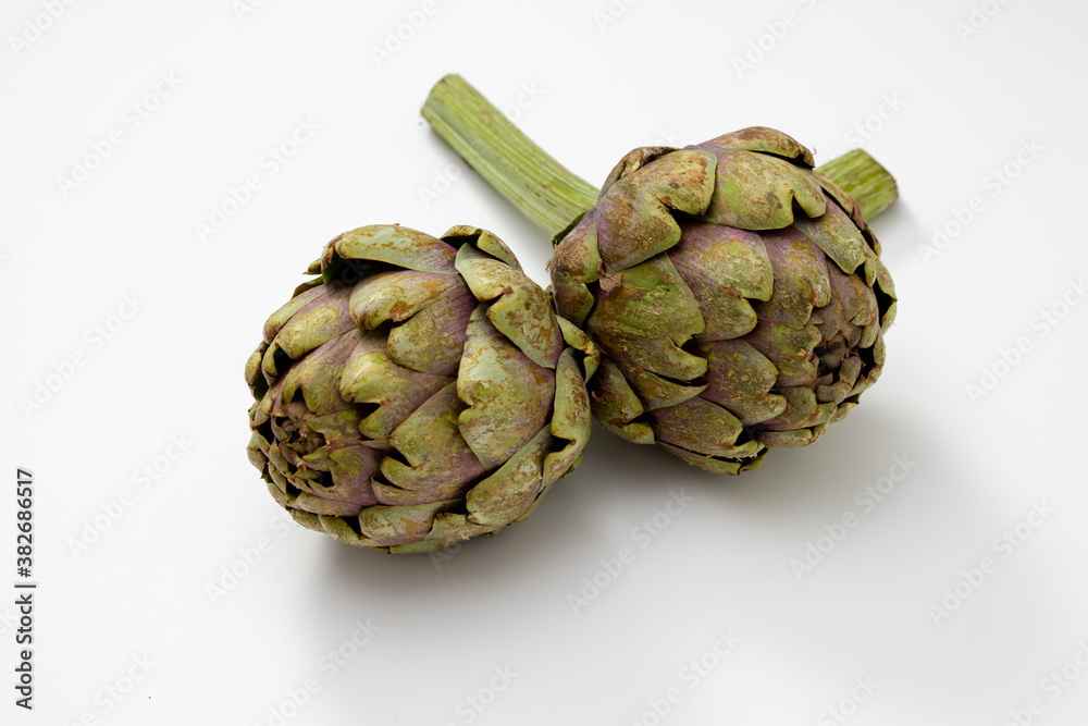Fototapeta premium Two organic artichokes with a piece of stem on a white surface.