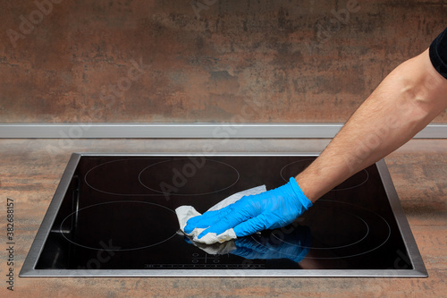 Adult man wipes dry the surface of an kitchen electric stove with a paper towel