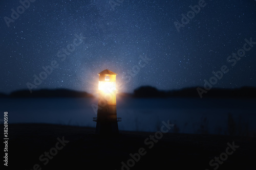 Small decorative lighthouse luminous in the dark. Lighthouse under the Milky Way. Light in the darkness.