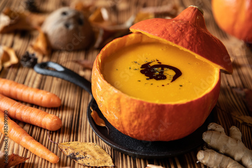 orange Suppe aus Kürbissen vom Hokkaido in einer Schale auf einem braunem Tisch aus Holz im Herbst zu Halloween