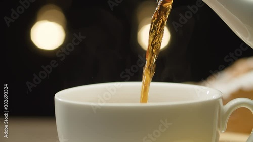 Close-up hot tea pouring into a cup on black background. Steam rises above the cup. Macro shot with slide or move camera. Dolly shot