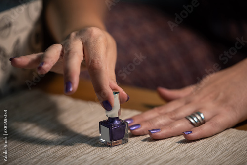 The woman is painting her nails purple, close up