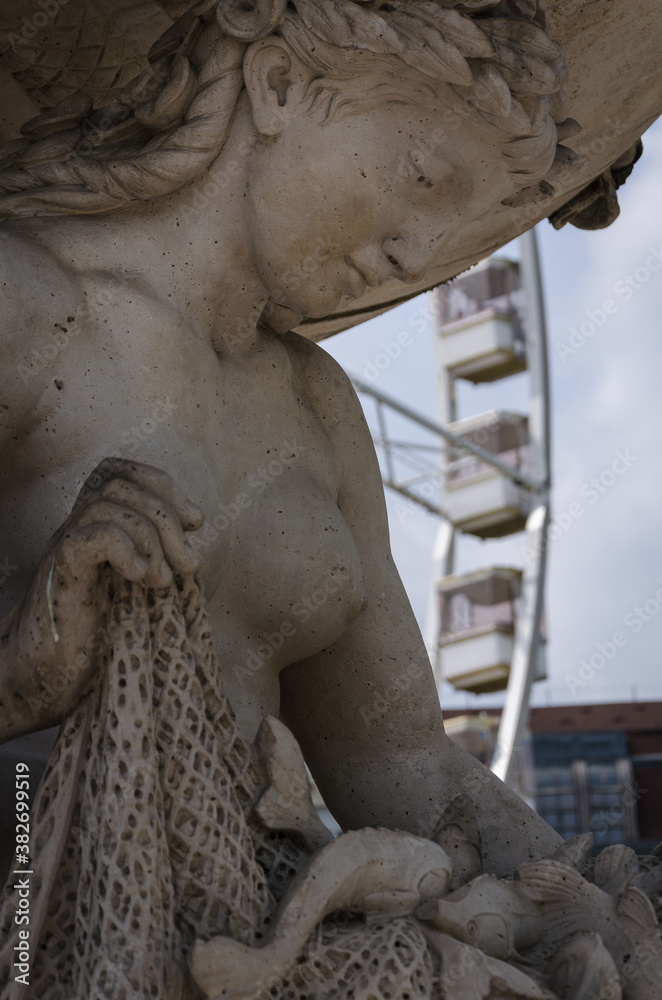 A statue representing to a fisher woman with a fishing net in her hands and some fishes trapped on it and the Budapest Eye in the background, Budapest, Hungary