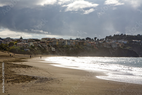 Windy day on Baker Beach near Golden Gate bridge, San Francisco, California. Tourists walking on beach with warm light before sunset. photo