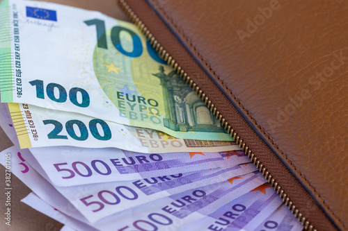 100, 200, 500 euro banknotes under a brown wallet, closeup


