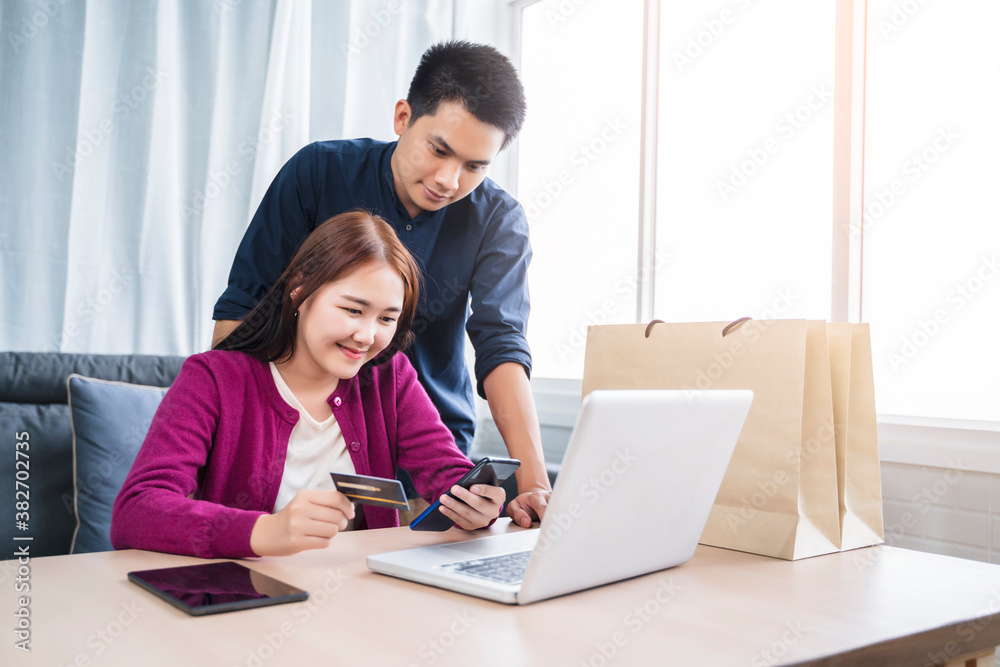 Asian couple online shopping ecommerce together from home modern living room using phone computer laptop tablet payment paying transaction money transfer credit debit card smiling happy joyfully Asian couple online shopping ecommerce together from home modern living room using phone computer laptop tablet payment paying transaction money transfer credit debit card smiling happy joyfully