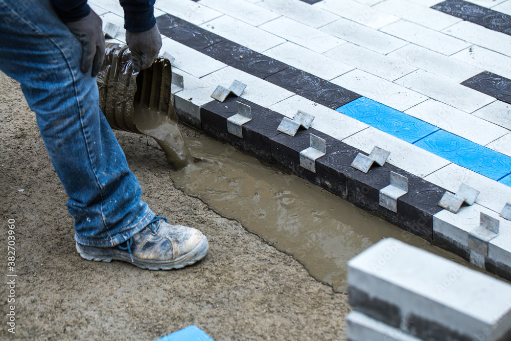 Construction work on pavement. Installation of concrete paver blocks on the sidewalk. Worker pours concrete mortar onto pre-prepared surface. Worker pours concrete mortar onto pre-prepared surface. Construction work on pavement. Installation of concrete paver blocks on the sidewalk. Worker pours concrete mortar onto pre-prepared surface. Worker pours concrete mortar onto pre-prepared surface.