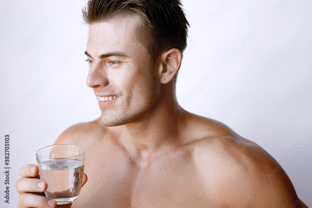 Muscular sexy model sports young man on white background. Portrait of beautiful smiling healthy guy holding a glass of water. Muscular sexy model sports young man on white background. Portrait of beautiful smiling healthy guy holding a glass of water.