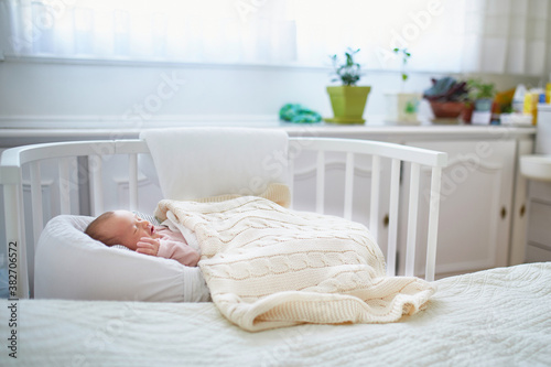 Newborn baby having a nap in co-sleeper crib attached to parents' bed