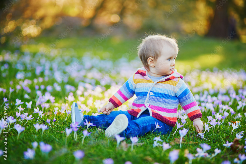 Baby girl in knitted clothes sitting on the grass with blue hyacinths