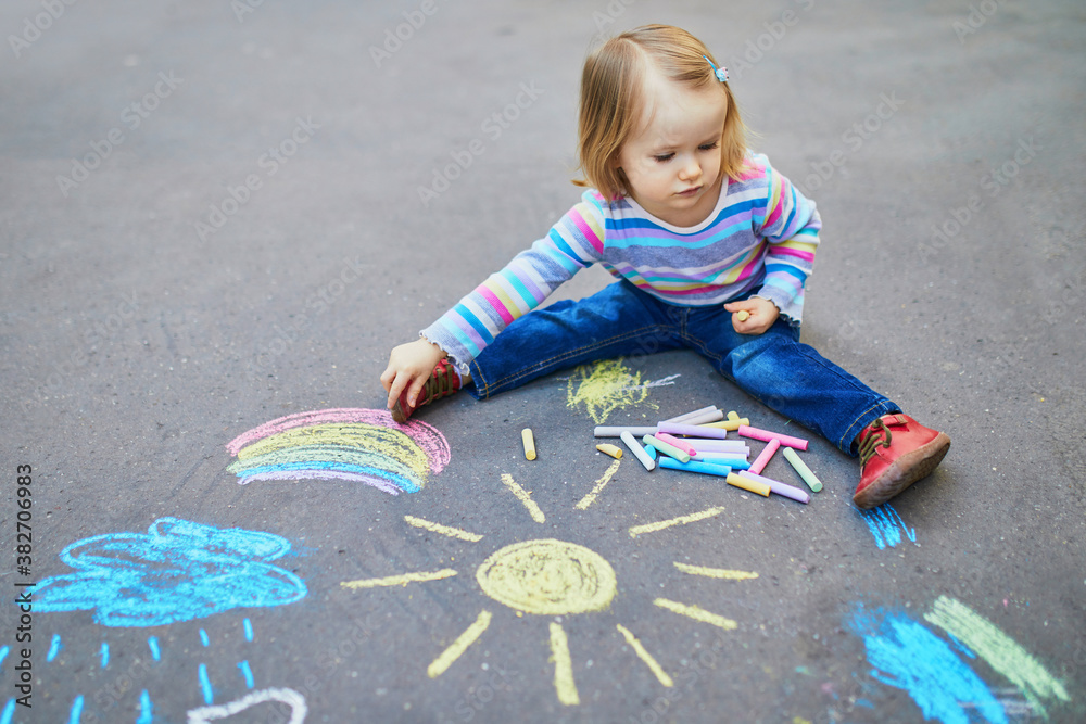 Fototapeta premium Adorable toddler girl drawing with colorful chalks on asphalt
