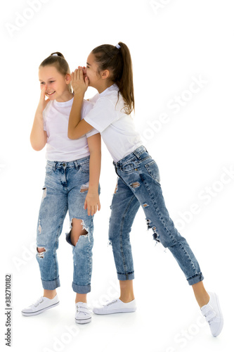Two cheerful little girls share secrets in each other s ear.