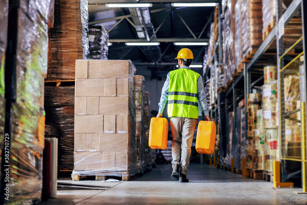 Worker in vest relocating cans with oil while walking in warehouse. Worker in vest relocating cans with oil while walking in warehouse.