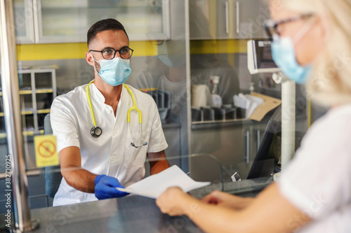 Young medical worker with rubber gloves  facial mask  in sterile uniform giving test results to a patient while sitting in laboratory.