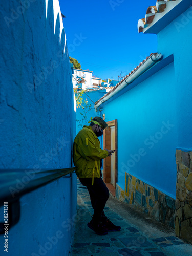 Hombre joven usando su teléfono móvil apoyado en una pared azul en Júzcar, Málaga. Andalucía, España