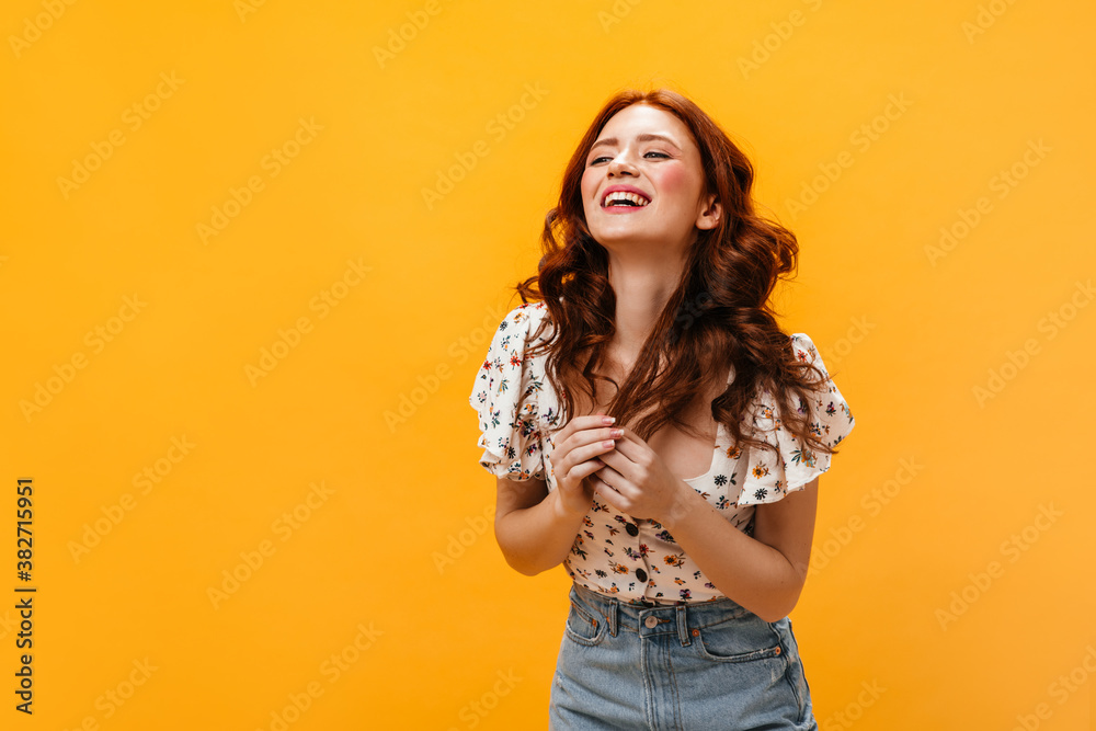 Woman in floral print top laughs and touches her wavy red hair coquettishly on orange background Woman in floral print top laughs and touches her wavy red hair coquettishly on orange background
