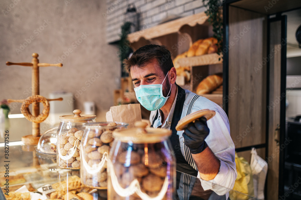 Handsome middle age male worker with protective mask on face working in bakery.