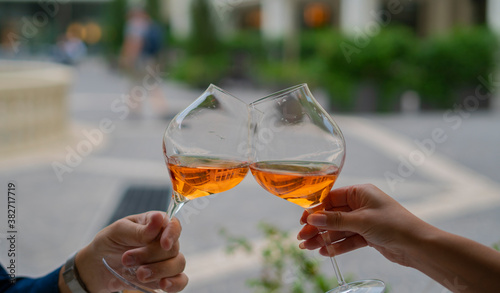 young couple toasting with glasses of rosé wine at the table outside the restaurant.