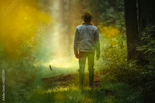 Man in denim jacket in forest during dreamy sunrise with sun rays shining trough the forest.