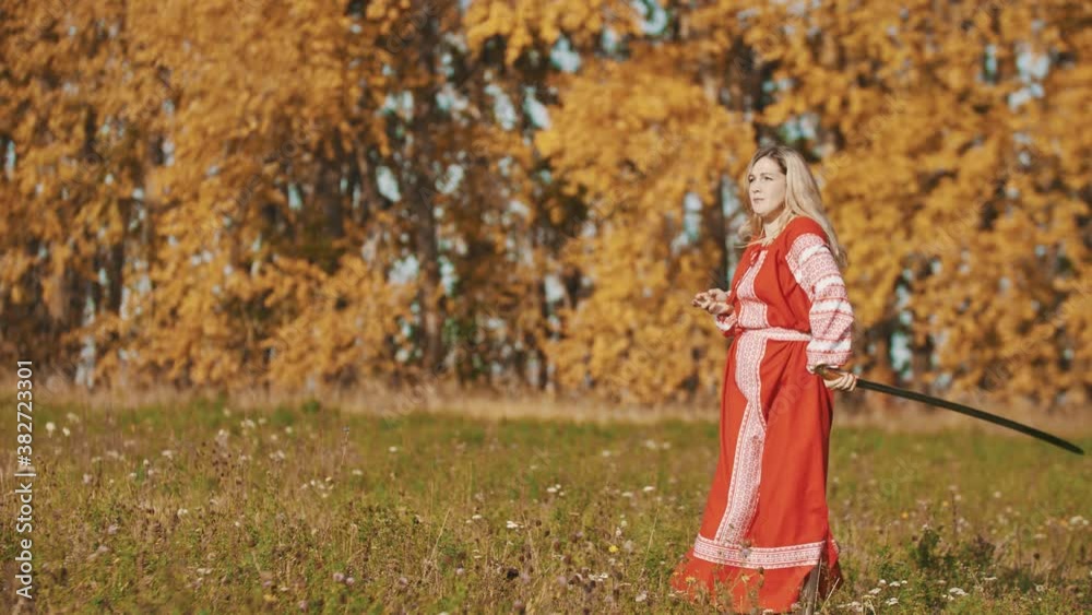 Strong woman in red national dress standing on the field and fencing with a sword Strong woman in red national dress standing on the field and fencing with a sword
