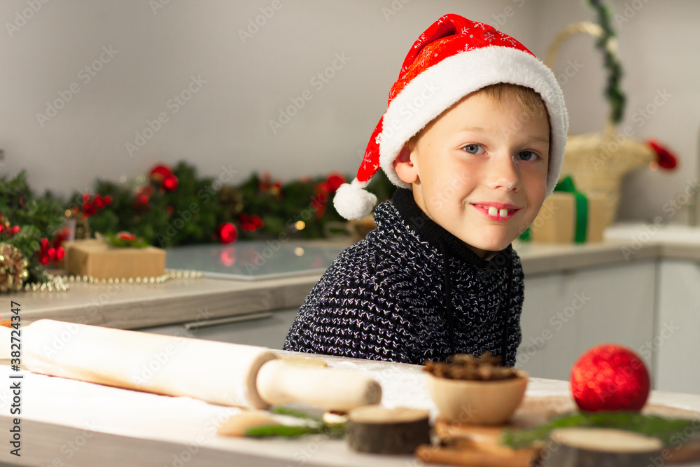 Boy 7-10 in a Christmas Santa's cap makes Christmas gingerbread cookies in the New Year's kitchen.