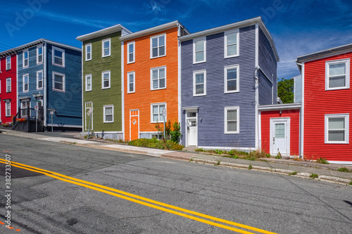 Street view of multiple colorful wooden buildings of various colors. The small structures have double-hung windows and white doors. There's a blue sky in the background.  A street is in the foreground © Dolores  Harvey