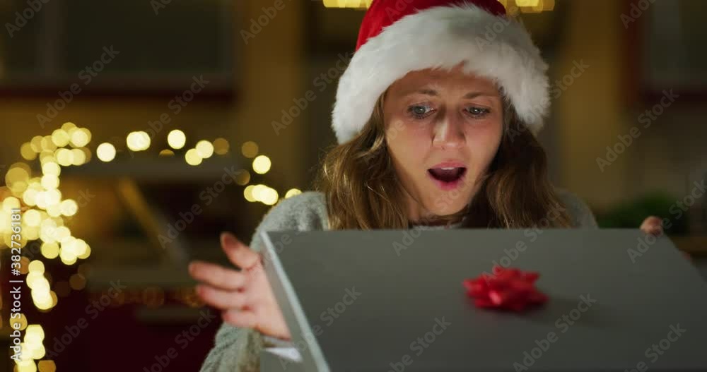 Authentic shot of happy young woman is opening her Christmas present box is excited and surprised with received gift. Concept: winter holidays, tradition, surprise, e-commerce