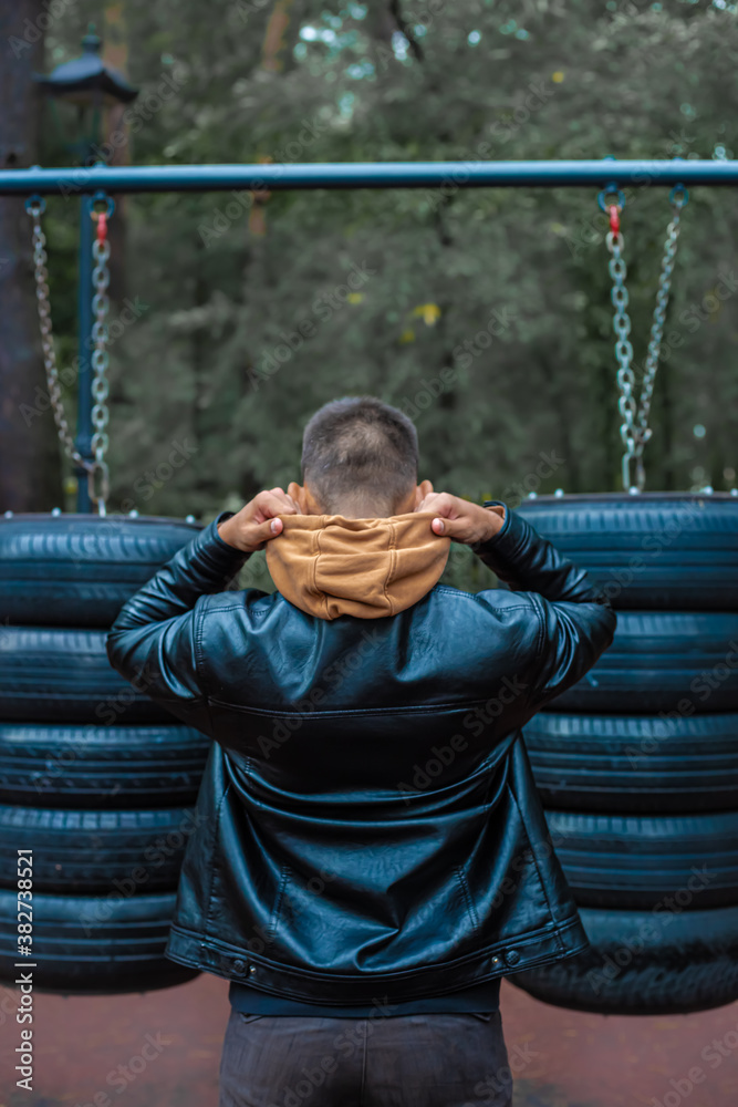 Obraz premium Young man pulling up, warming up on street workout area. Physical activity outdoors, caucasian man with tanned skin training, cloudy cold day, sport casual clothes