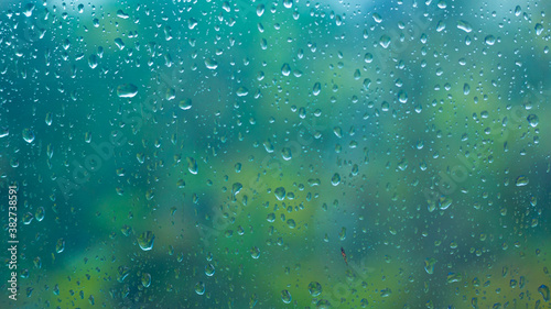 horizontal soft focused or blurred rainy window background. raindrops on the clear window glass, rainy day, blue and green background, evening light