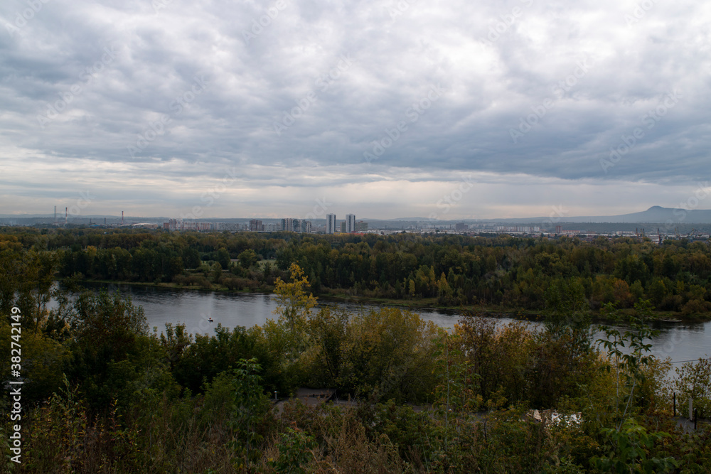 Fototapeta premium Panoramic view of the river with the city on the horizon, on a cloudy day.