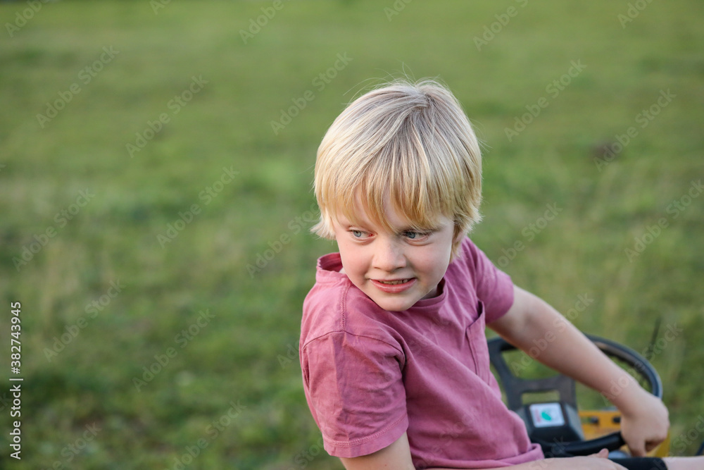 Boy sitting on lawn mower in field smiling Boy sitting on lawn mower in field smiling