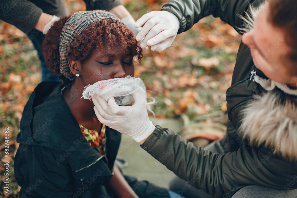 Fototapeta premium Guys help a woman. African girl sitting unconscious. Providing first aid in the park