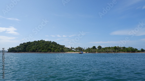 A small island with many trees on it. A small green island under the blue sky with blue ocean around it.