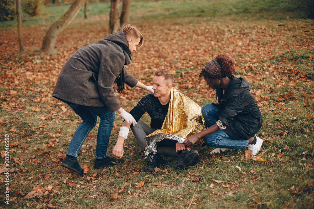 Friends help the guy. The wounded boy sitting on the ground. Providing first aid in the park. Friends help the guy. The wounded boy sitting on the ground. Providing first aid in the park.