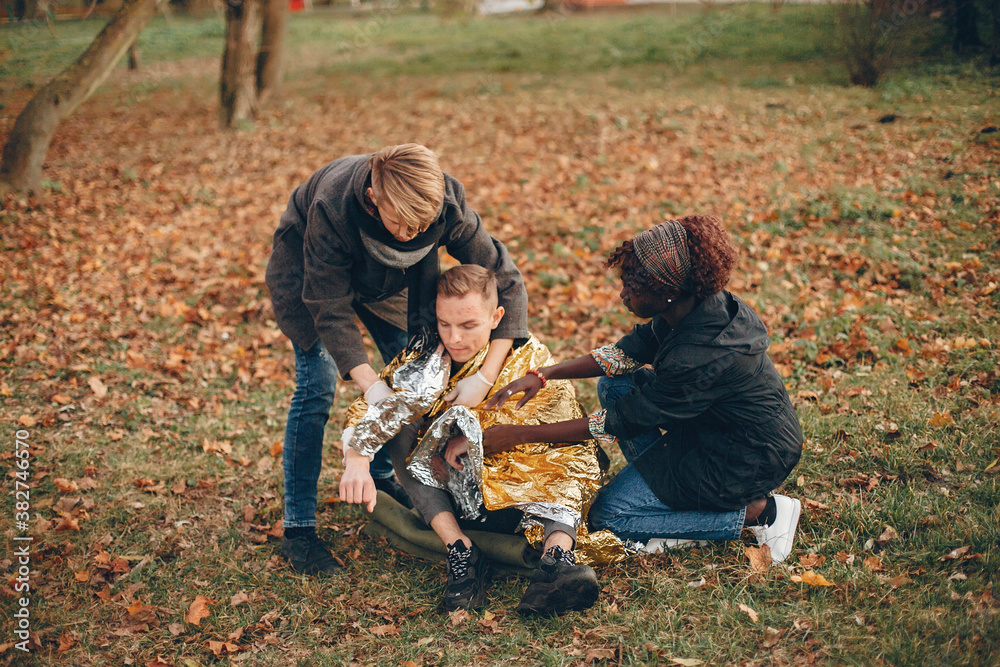 Friends help the guy. The wounded boy sitting on the ground. Providing first aid in the park. Friends help the guy. The wounded boy sitting on the ground. Providing first aid in the park.