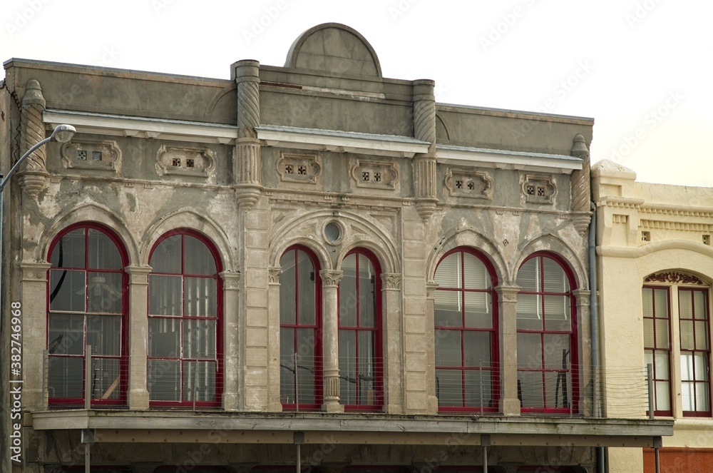 Second story view of historic stone building on Galveston Island, Texas, with tall, arched windows with red frames, balcony porch and awning, and ceiling fan - obrazy, fototapety, plakaty 