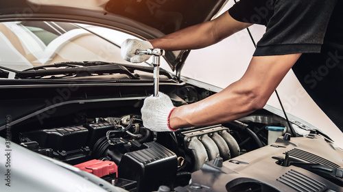 Close-up hands of auto mechanic are using the wrench to repair a car engine in auto car garage. Concepts of car care fixed repair and services.
