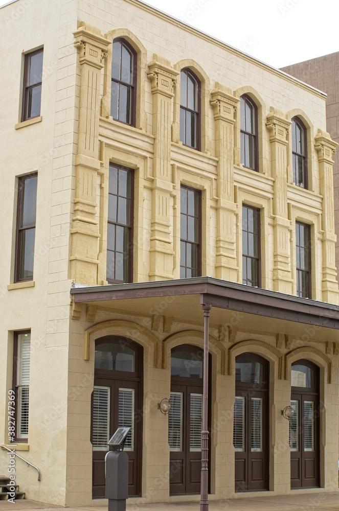 Vertical: Historic stone building in Galveston Island, Texas with tall windows, brown doors, and awning
