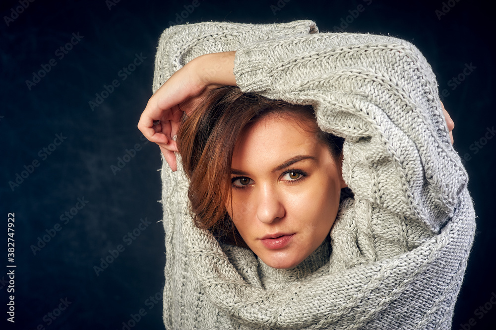 Obraz premium Portrait of a young beautiful girl in a warm knitted sweater on a dark background